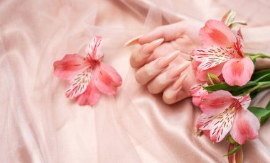 Zarif pastel pembe doğal manikür. Pembe ipek arka planda çiçekli kadın elleri..
