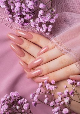 Güzel manikürlü, pembe ipekli çingene çiçekli kadın elleri.