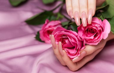 Pembe tırnak desenli kadın elleri pembe gülleri tutuyor. Pembe arka planda pembe oje manikürü.