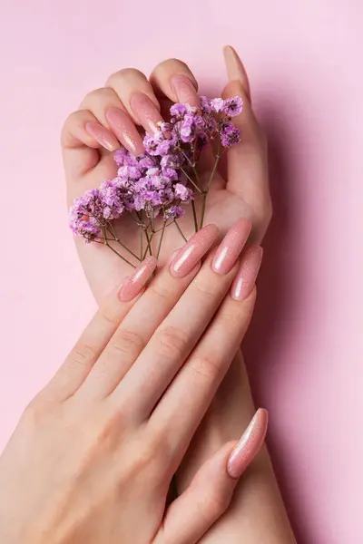 Female hands with pink nail design  hold gypsophila flowers. Pink nail polish manicure on pink background