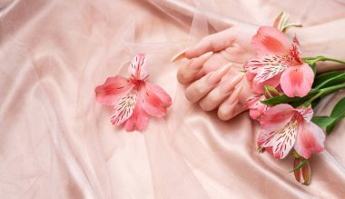 Zarif pastel pembe doğal manikür. Pembe ipek arka planda çiçekli kadın elleri..