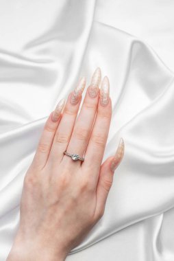 İpek arka planda beyaz inci manikürlü genç bir kadının eli. 