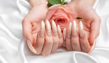 Güzel inci manikürlü ve pembe gül çiçekli beyaz ipek arka planda kadın elleri