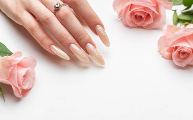 Güzel inci manikürlü ve pembe gül çiçekli beyaz bir zemin üzerinde kadın elleri
