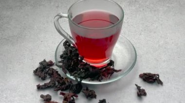 Cam bir fincanda kırmızı amber çayı ve masada kurutulmuş amber çiçeği.