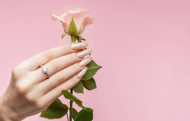 Cilt bakımı. Pembe güllü eller. İnci manikürlü güzel kadın tırnakları ve pembe arka planda gül.