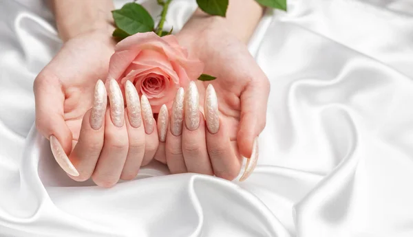 Female Hands on a white silk background with beautiful pearl manicure and pink rose flowers