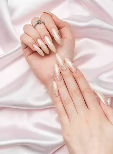 Female Hands on a white folded silk background with beautiful pearl manicure