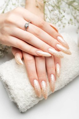 İnci ojeli manikürlü tırnaklar. Tırnaklar beyaz arka planda inci jölesiyle kaplanmış.