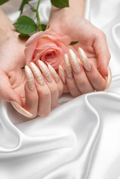 Female Hands on a white silk background with beautiful pearl manicure and pink rose flowers