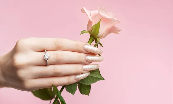 Skin care. Hands with pink rose.   Beautiful woman\'s nails with  pearl manicure and rose on pink background