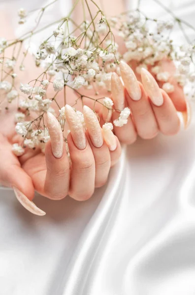 Female Hands on a white silk background with beautiful pearl manicure and gypsophila flowers