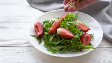 Çilek ve roka salatasına çam fıstığı serpiştiren bir kadın eli. Yaz salatası hazırlığı