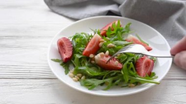 Yaz salatası hazırlığı. Bir kadının eli çatallı çilek ve roka salatası seçiyor.