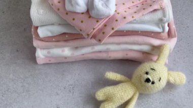 Bebek kıyafetleri yığını. Çocuk tulumunun yanında bebek örgü tavşan oyuncağı var.