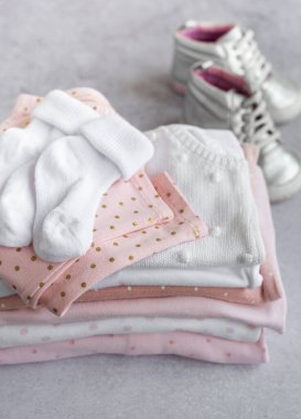 Gri bir arka planda bebek kıyafetleri yığını. Çocuklar için tulumun yanındaki bebek ayakkabıları. 