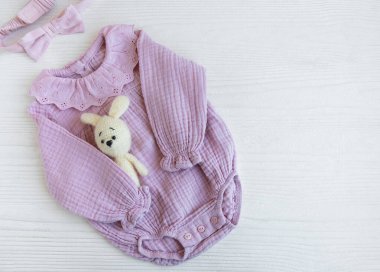 Oyuncak örülü oyuncak ve saç bandıyla pembe bir beden. Yazın beyaz ahşap arka planda bebek kıyafetleri ve aksesuarlar. Yeni doğan moda. Düz yatış, üst yaşam
