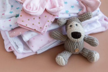 Bebek kıyafetleri yığını. Yavru örülmüş köpek oyuncağı, çocuklar için tulumların yanında.
