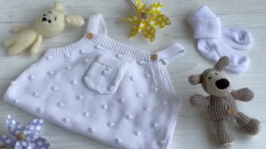 Yeni doğan bebek için beyaz kıyafetler ve aksesuarlar. Örgü oyuncaklar, örgü şamata, beyaz ahşap arka planda çoraplar. Bebek partisi konsepti. Düz yatış, üst görünüm