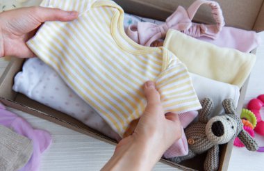 Kadın elleri çocuk kıyafetlerini kutulara toplar. Bir çocuğun doğumuna ya da bağışına hazırlık konsepti.