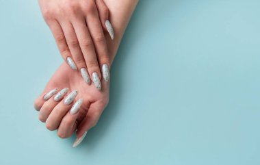 Mavi pastel arka planda mavi tırnak desenli kadın elleri. Mavi oje manikür.. 