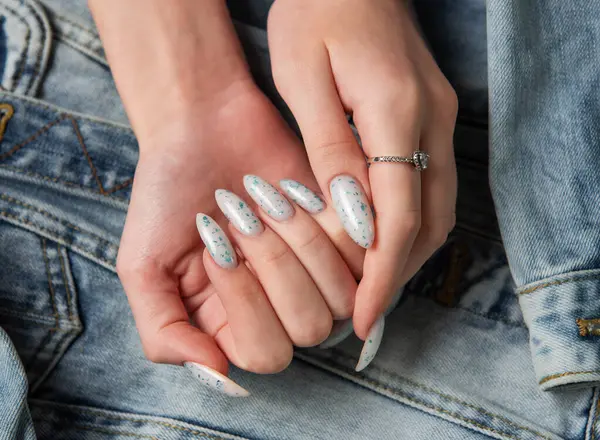 Female hands with blue nail design on blue jeans background. Blue nail polish manicure.