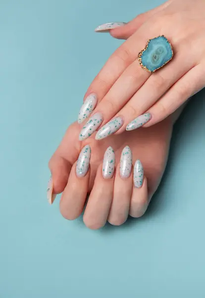 Female hands with blue nail design on blue pastel background. Blue nail polish manicure.
