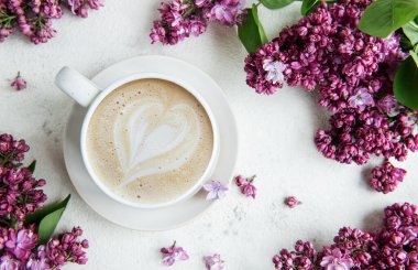 Bir fincan kahveyle latte sanat ve leylak çiçekleri. 