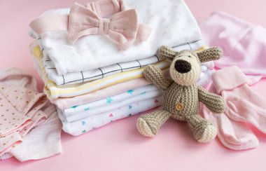 Bebek kıyafetleri yığını. Yavru örülmüş köpek oyuncağı, çocuklar için tulumların yanında.