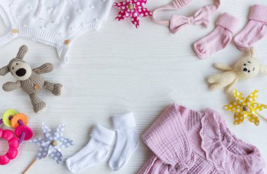 Yeni doğan bebek için pembe kıyafetler ve aksesuarlar. Örgü oyuncaklar tavşan ve köpek, romper, çoraplar ve beyaz ahşap arka planda el bandı. Bebek partisi konsepti. Düz yatış, üst görünüm
