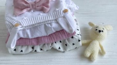 Bebek kıyafetleri yığını. Çocuk tulumunun yanında bebek örgü tavşan oyuncağı var.