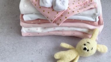 Bebek kıyafetleri yığını. Çocuk tulumunun yanında bebek örgü tavşan oyuncağı var.