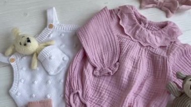 Yeni doğan bebek için pembe kıyafetler ve aksesuarlar. Örgü oyuncaklar tavşan ve köpek, romper, çoraplar ve beyaz ahşap arka planda el bandı. Bebek partisi konsepti. Düz yatış, üst görünüm