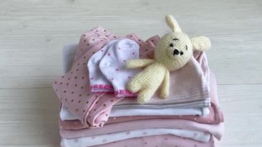 Bebek kıyafetleri yığını. Çocuk tulumunun yanında bebek örgü tavşan oyuncağı var.