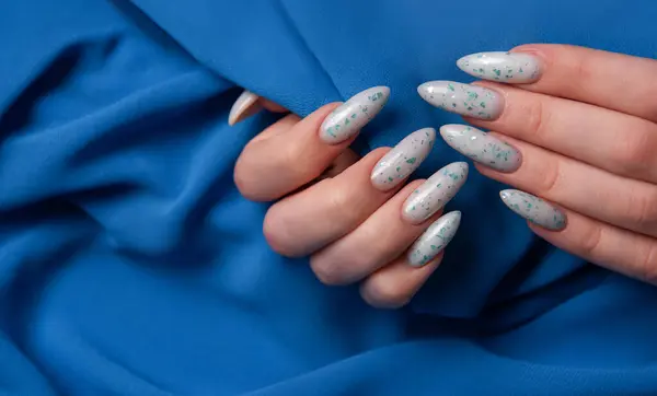 Female hands with blue nail design on blue textile background. Blue nail polish manicure.