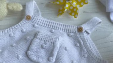 Yeni doğan bebek için beyaz kıyafetler ve aksesuarlar. Örgü oyuncaklar, örgü şamata, beyaz ahşap arka planda çoraplar. Bebek partisi konsepti. Düz yatış, üst görünüm