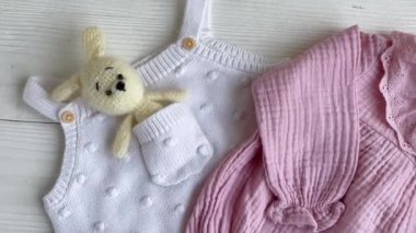 Yeni doğan bebek için pembe kıyafetler ve aksesuarlar. Örgü oyuncaklar tavşan ve köpek, romper, çoraplar ve beyaz ahşap arka planda el bandı. Bebek partisi konsepti. Düz yatış, üst görünüm