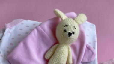 Bebek kıyafetleri yığını. Çocuk tulumunun yanında bebek örgü tavşan oyuncağı var.