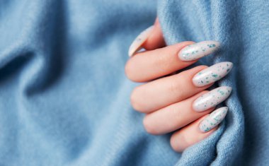 Mavi tekstil arka planında mavi tırnak desenli kadın elleri. Mavi oje manikür.. 