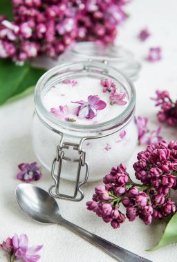 Gümüş tokalı şeffaf bir cam kavanoz, narin mor çiçeklerle süslenmiş ev yapımı eflatun şekerle doldurulur. Taze leylak çiçekleri kavanozun etrafını sarar. Tüylü beyaz bir yüzey üzerinde dinlenir. Bahar aşçılığı hazırlığını işaret eder..