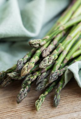 Bir grup yeni toplanmış kuşkonmaz düzgün bir şekilde sade ahşap bir masaya dizilmiştir. Yeşil ve mor renkleri yumuşak, doğal gün ışığıyla hafifçe vurgulanmıştır..