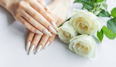 Güzel inci manikürlü ve beyaz gül çiçekli beyaz arka planda kadın elleri