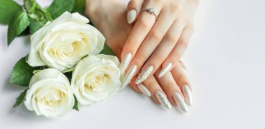 Güzel inci manikürlü ve beyaz gül çiçekli beyaz arka planda kadın elleri