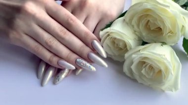 Güzel inci manikürlü beyaz arka planda kadın elleri ve beyaz güller.