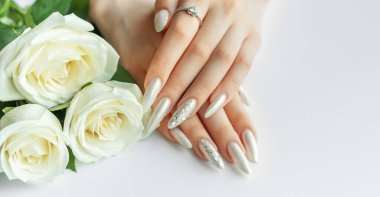 Güzel inci manikürlü ve beyaz gül çiçekli beyaz arka planda kadın elleri