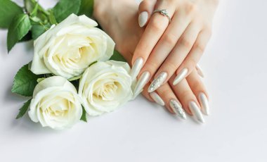 Güzel inci manikürlü ve beyaz gül çiçekli beyaz arka planda kadın elleri