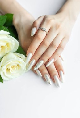 Beyaz bir zemin üzerinde kadın elleri Güzel bir inci manikür ve beyaz gül