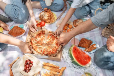 Aile piknikte. Birkaç el pizza alır, yukarısı görünür.