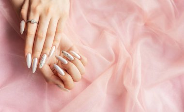 Pembe arka planda güzel inci manikürlü kadın elleri.