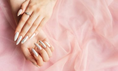 Pembe arka planda güzel inci manikürlü kadın elleri.